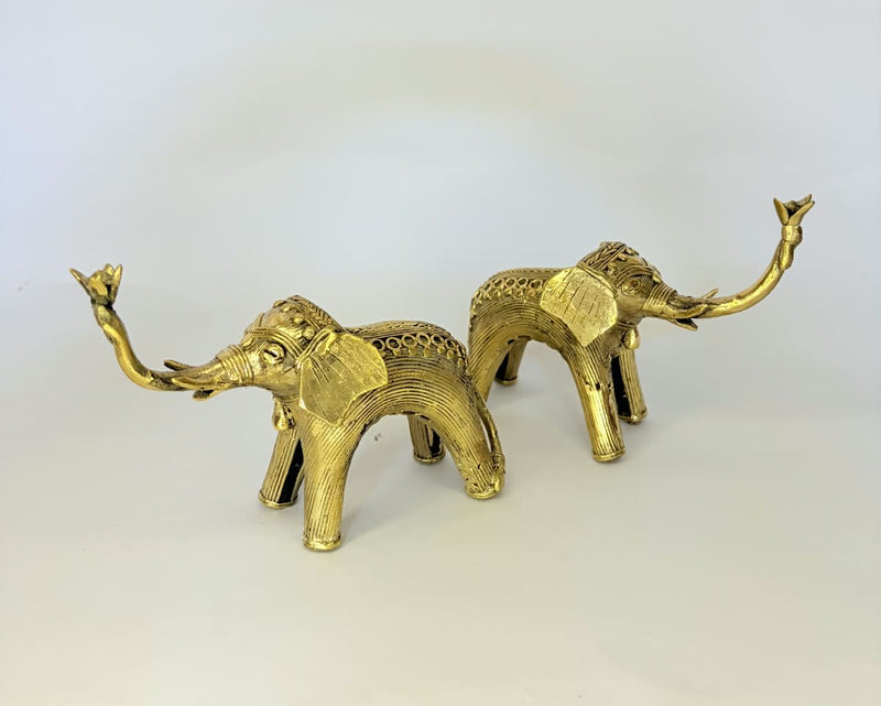 A pair of small brass elephant figurines with raised trunks, displayed on a plain light gray background.